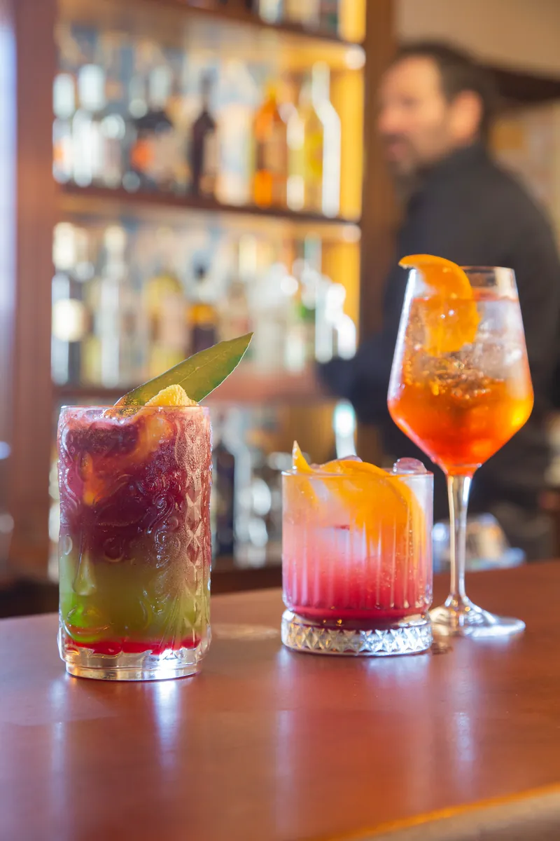 Tre cocktail pronti sul bancone, il barman dietro